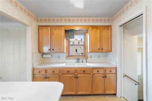 kitchen featuring wallpapered walls, light countertops, brown cabinetry, and a sink