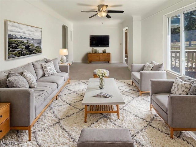 living area featuring baseboards, arched walkways, ceiling fan, and carpet flooring