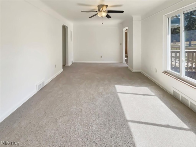 carpeted spare room with arched walkways, visible vents, baseboards, and ceiling fan