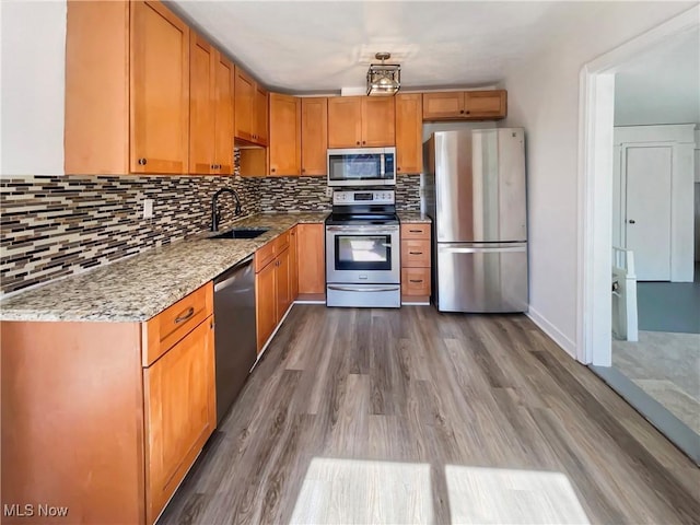 kitchen with a sink, light stone counters, backsplash, wood finished floors, and appliances with stainless steel finishes