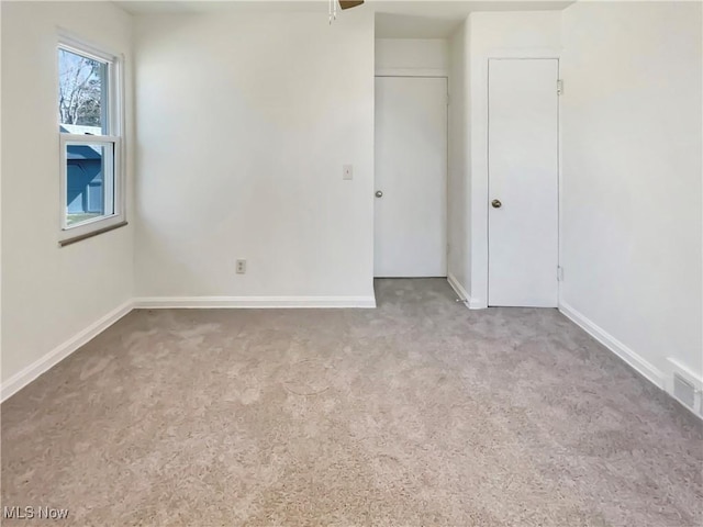 carpeted spare room with visible vents, baseboards, and a ceiling fan