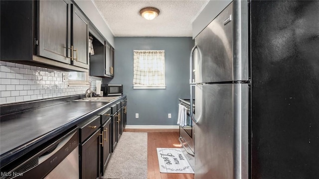 kitchen featuring a sink, stainless steel appliances, light wood-style floors, dark countertops, and tasteful backsplash