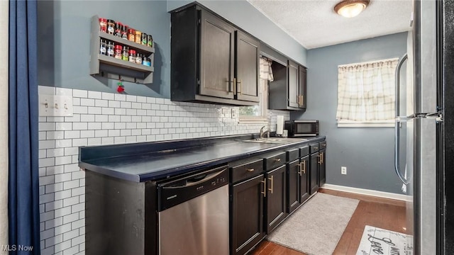 kitchen featuring refrigerator, a sink, dark wood-type flooring, dishwasher, and dark countertops