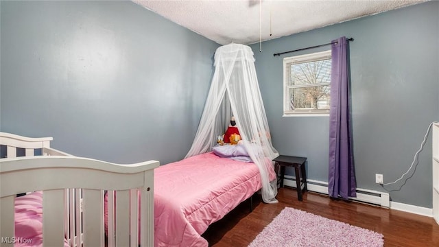 bedroom featuring a textured ceiling, a baseboard heating unit, baseboards, and wood finished floors