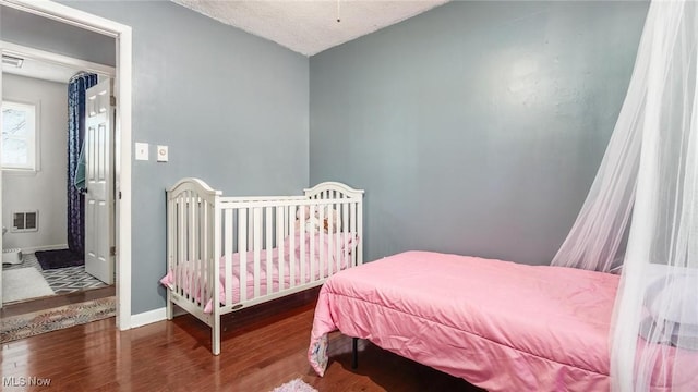 bedroom with a textured ceiling, wood finished floors, visible vents, and baseboards