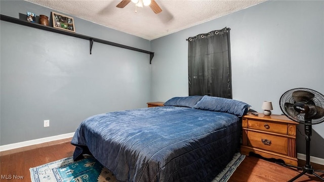 bedroom featuring ceiling fan, a textured ceiling, baseboards, and wood finished floors