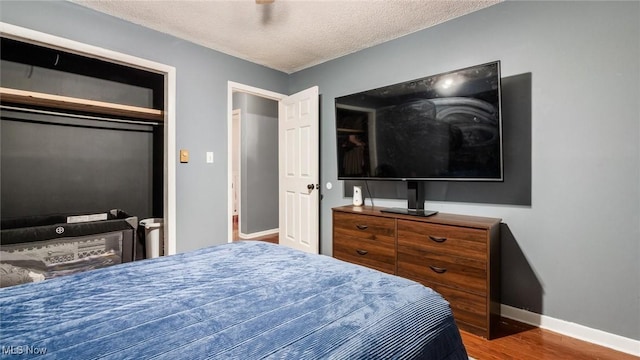 bedroom with a closet, a textured ceiling, baseboards, and wood finished floors