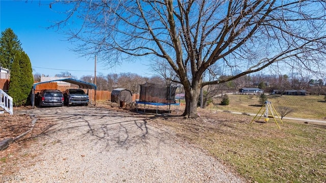 view of yard featuring a trampoline, a carport, driveway, a storage unit, and an outbuilding