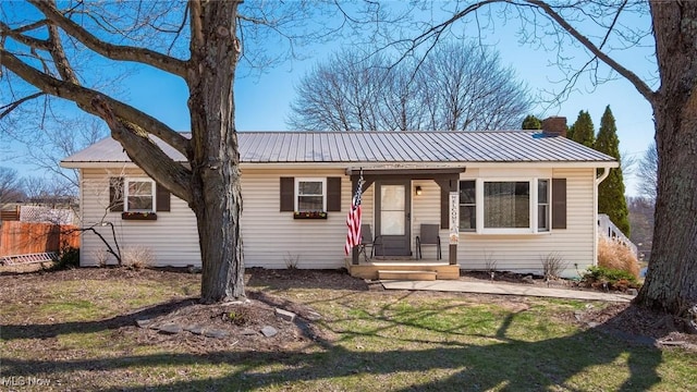 view of front of house with metal roof, a front yard, a chimney, and fence