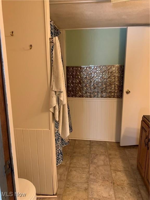 full bath with a wainscoted wall, toilet, and vanity