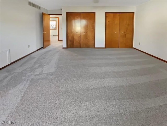 unfurnished bedroom with visible vents, multiple closets, baseboards, and light carpet