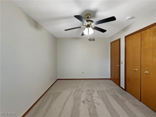 unfurnished bedroom featuring baseboards, visible vents, ceiling fan, light carpet, and two closets