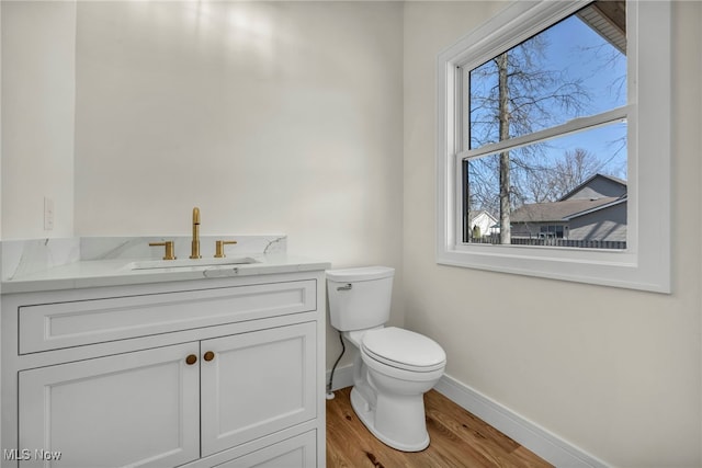 half bath featuring plenty of natural light, toilet, vanity, and baseboards