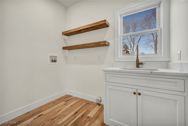 laundry area featuring light wood-style flooring, a sink, cabinet space, baseboards, and hookup for a washing machine