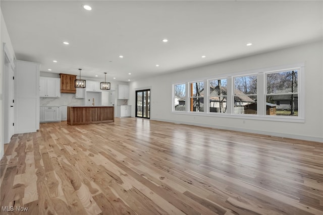 unfurnished living room with recessed lighting, light wood-type flooring, and baseboards