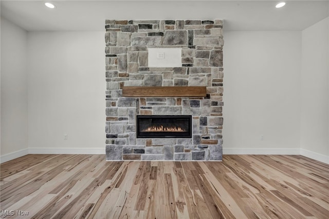 unfurnished living room featuring baseboards, a stone fireplace, and wood finished floors