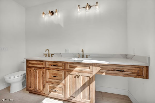 bathroom featuring double vanity, toilet, baseboards, and a sink