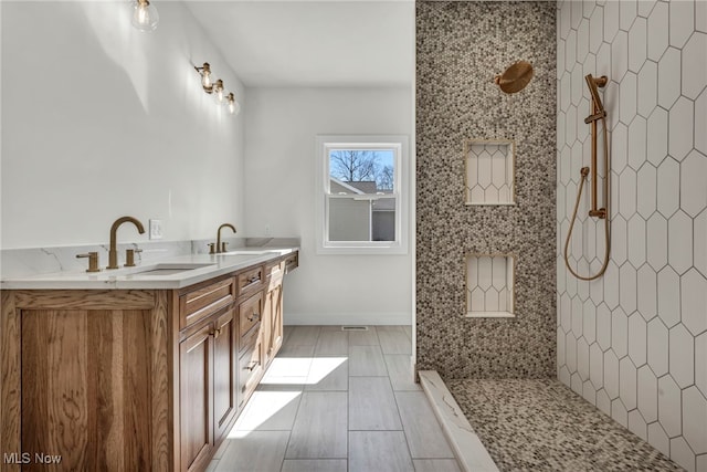 bathroom with a sink, baseboards, double vanity, and a tile shower