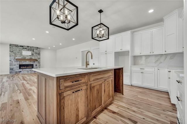 kitchen featuring a notable chandelier, a sink, white cabinetry, a fireplace, and light wood finished floors