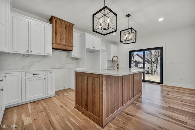 kitchen with light wood-type flooring, decorative backsplash, an inviting chandelier, white cabinets, and a kitchen island with sink