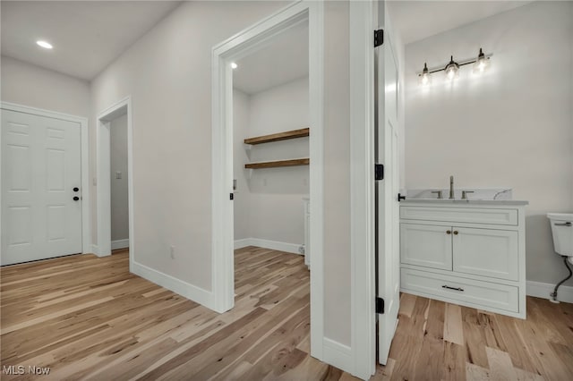 hall with light wood-style flooring, baseboards, and a sink