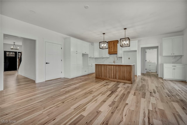 kitchen featuring light wood-type flooring, a notable chandelier, an island with sink, a sink, and white cabinets