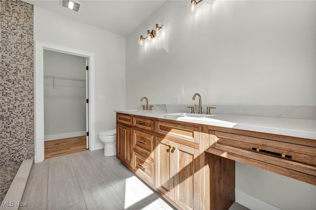 full bathroom featuring visible vents, double vanity, a sink, a walk in closet, and toilet