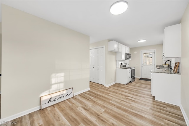 kitchen featuring a sink, white cabinetry, stainless steel appliances, light wood-style floors, and baseboards