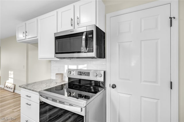 kitchen featuring light wood-type flooring, tasteful backsplash, white cabinetry, stainless steel appliances, and light stone countertops