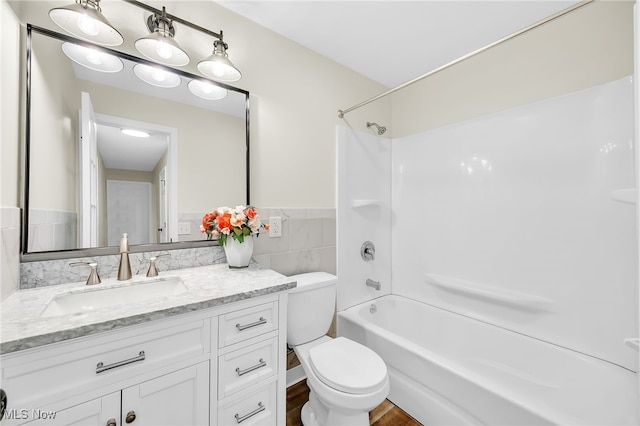 bathroom with vanity,  shower combination, wainscoting, tile walls, and toilet