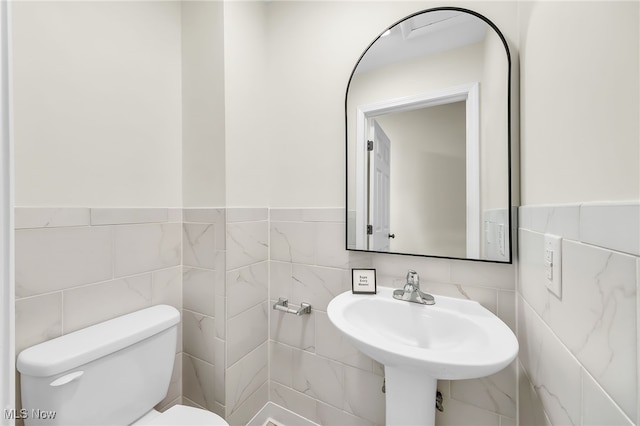 half bath featuring a sink, toilet, and tile walls