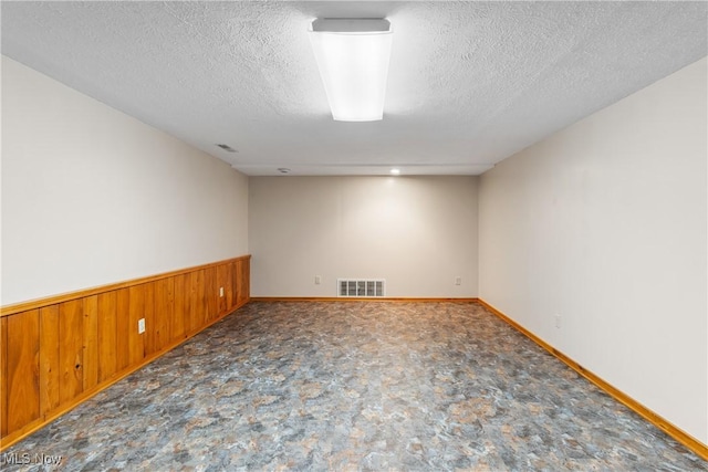 spare room with visible vents, wooden walls, wainscoting, and a textured ceiling