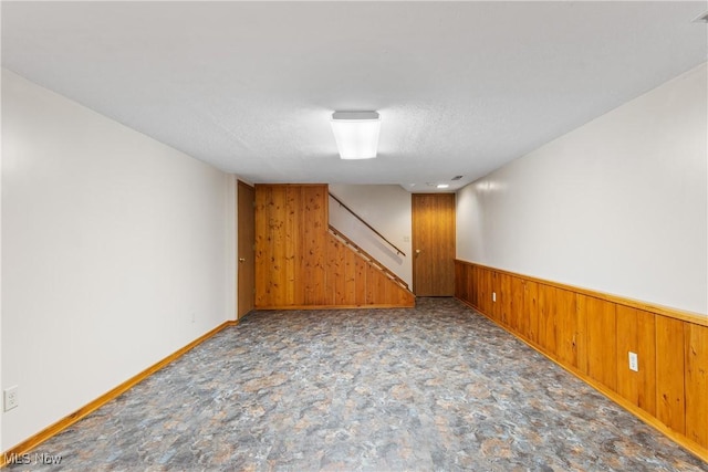 unfurnished room with baseboards, wood walls, stairs, wainscoting, and a textured ceiling