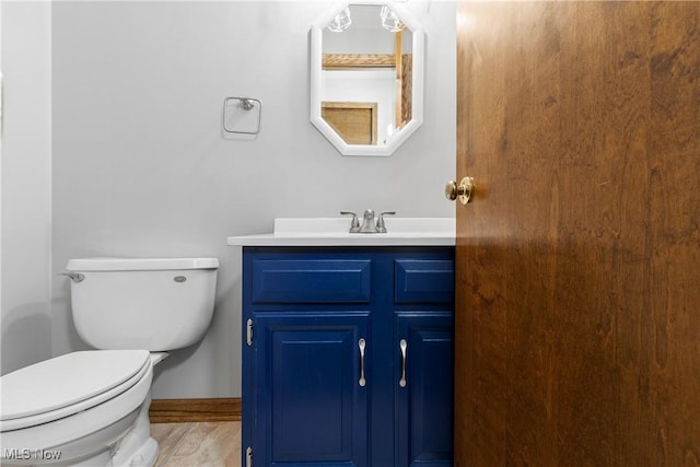 half bath featuring baseboards, toilet, and vanity