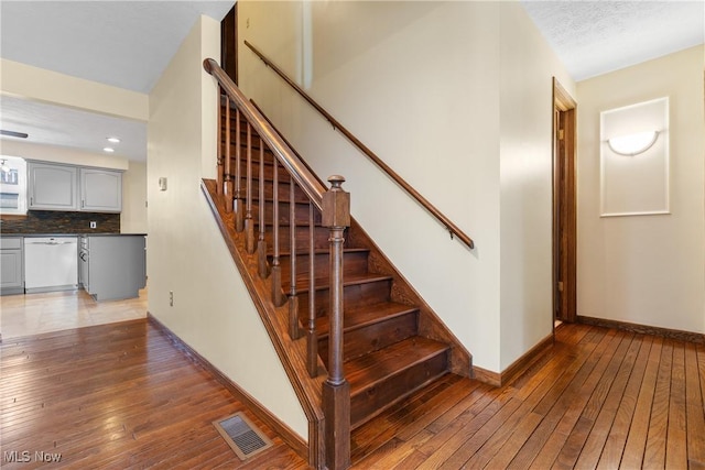 stairway with visible vents, baseboards, a textured ceiling, and hardwood / wood-style floors