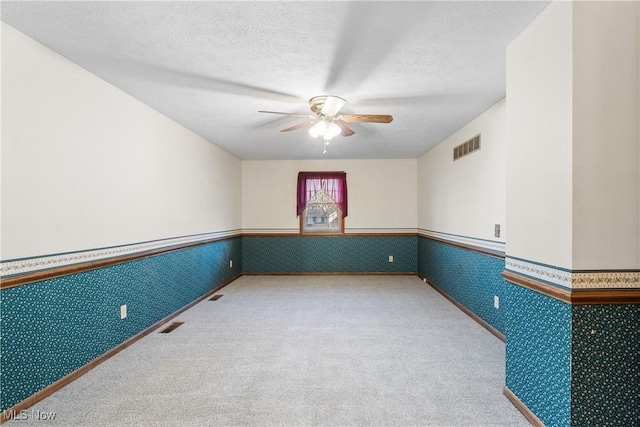 empty room with a ceiling fan, wainscoting, and wallpapered walls