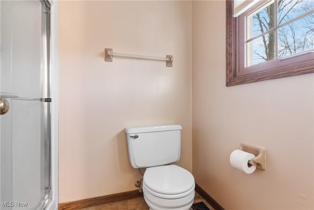 bathroom featuring a shower with shower door, baseboards, and toilet