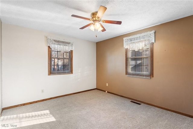 carpeted spare room featuring a wealth of natural light, visible vents, baseboards, and a ceiling fan