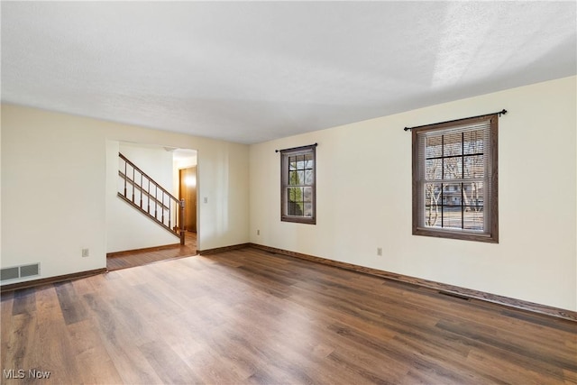 empty room with visible vents, stairway, baseboards, and wood finished floors