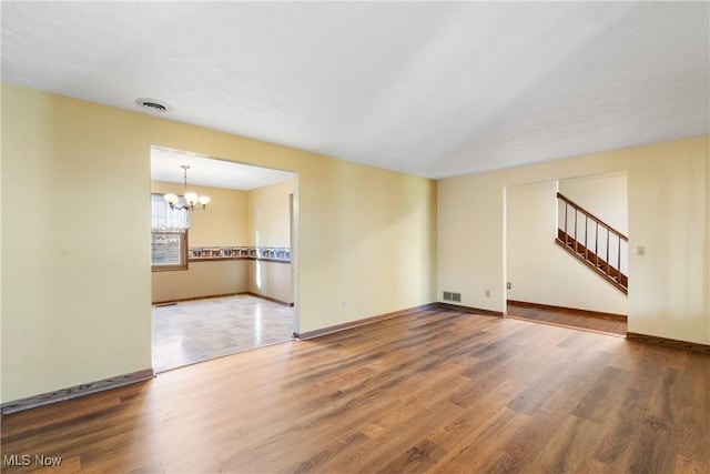 unfurnished living room featuring a chandelier, visible vents, baseboards, and wood finished floors