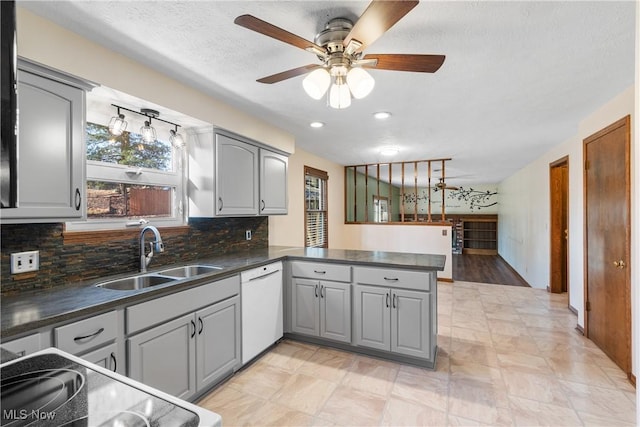 kitchen with gray cabinets, a sink, dark countertops, a peninsula, and dishwasher