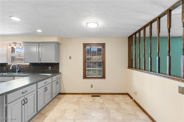 kitchen featuring backsplash, a healthy amount of sunlight, gray cabinetry, and a sink