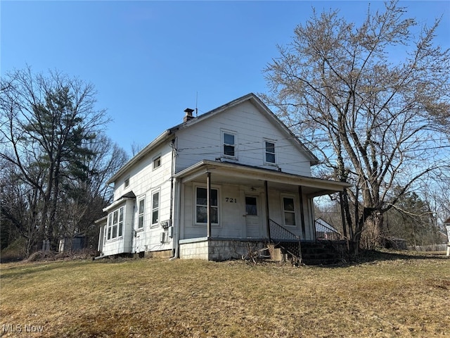 view of front of house with a chimney, covered porch, and a front lawn