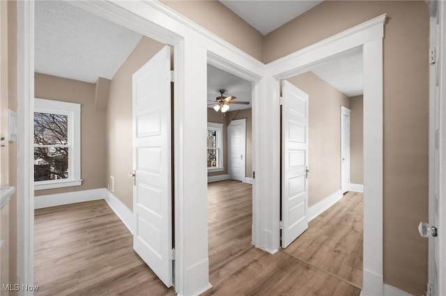 corridor featuring a wealth of natural light, baseboards, light wood finished floors, and a textured ceiling