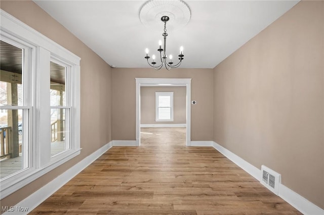 unfurnished dining area with baseboards, visible vents, light wood finished floors, and a chandelier