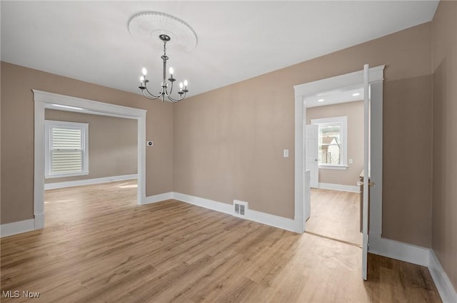 spare room featuring a notable chandelier, light wood-style floors, and baseboards