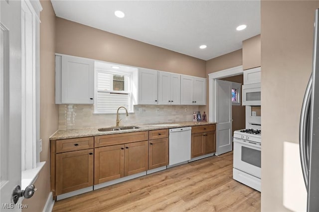 kitchen featuring white appliances, a sink, decorative backsplash, light wood-style floors, and brown cabinets