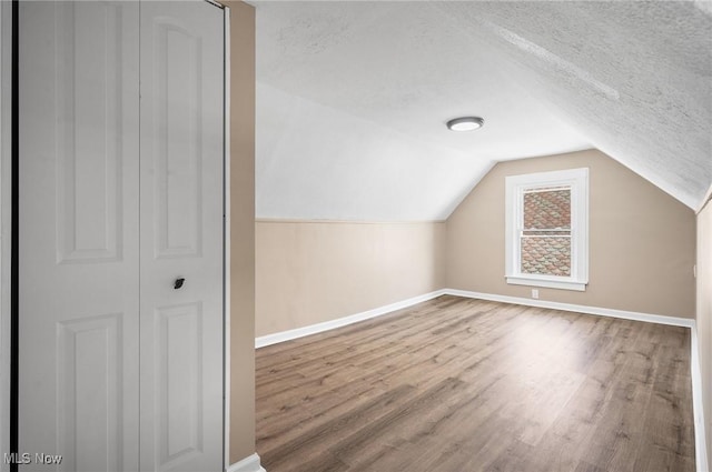 additional living space with lofted ceiling, wood finished floors, baseboards, and a textured ceiling