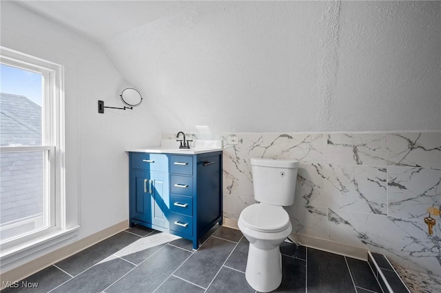 bathroom featuring tile patterned flooring, toilet, vanity, vaulted ceiling, and tile walls