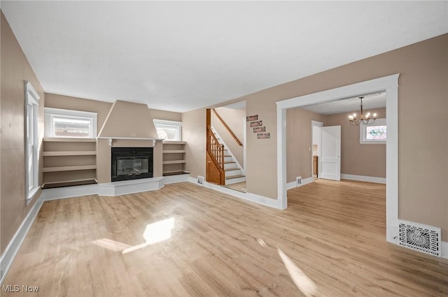 unfurnished living room with stairs, a notable chandelier, wood finished floors, and visible vents